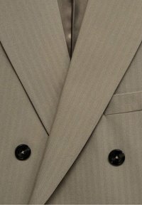 Blazer beige doppiopetto con bottoni neri, caratterizzato da un colletto a punta e una tasca sul petto a filetto.