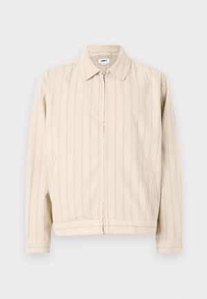 Beige Zip-Jacke mit vertikalen hellblauen Streifen. Verfügt über einen Kragen, zwei seitliche Taschen und einen geraden Saum. Hergestellt aus Baumwollstoff.