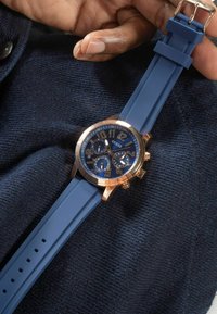 Sinine silikoonist rihmaga kell, millel on roosakuldne korpus, suur tumesinine nägu ning kronograafi alad julgete numbrite ja tähistustega.