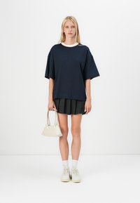 Námornícky oversized tričko s bielym golierom, v kombinácii s plisovanou čiernou sukňou. Drží malú krémovú kabelku. Biele tenisky a ponožky.