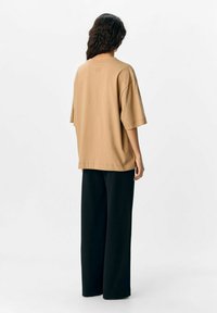 Overmaat beige katoenen t-shirt met korte mouwen en een logo op de rug, gecombineerd met loszittende zwarte broek. Zachte structuur en een relaxte pasvorm.