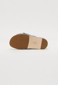 Sandale bleu clair avec un large design de sangle. La semelle est beige avec une finition lisse et présente un logo de la marque embossé près du talon.