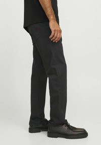 Pantalones de algodón negros con un diseño de pierna recta, con un pequeño acento rojo en el bolsillo trasero. Combinados con zapatos negros de cordones.