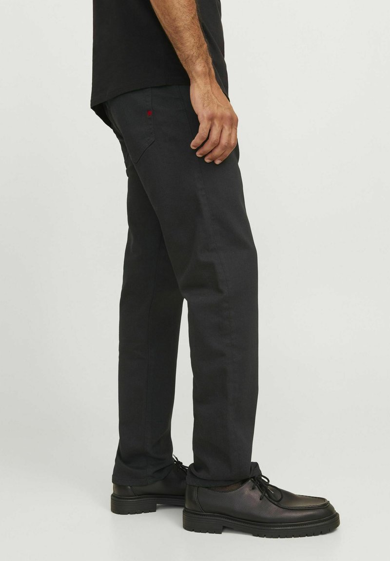 Pantalones de algodón negros con un diseño de pierna recta, con un pequeño acento rojo en el bolsillo trasero. Combinados con zapatos negros de cordones.