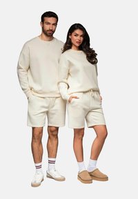 Vaalean beige rentoja asusteita, joissa on ylisuuret collegeshirtit ja niihin sopivat shortsit. Molemmat vaatekappaleet on valmistettu pehmeästä kankaasta.