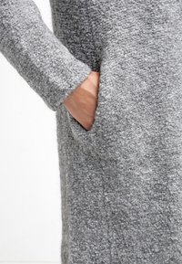 Vestido gris texturizado con mangas largas y bolsillos laterales, que presenta un material suave y difuso y un diseño de corte relajado.