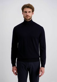 Marinefarbener Rollkragenpullover aus weichem, feinem Strickmaterial. Mit langen Ärmeln und einer figurbetonten Saumabschlüsse. Getragen mit dunklen Hosen.
