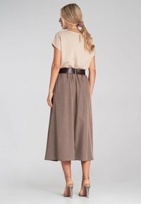 Beżowa bluzka z krótkimi rękawami w połączeniu z brązową, zwiewną spódnicą o wysokim stanie, podkreśloną szerokim czarnym paskiem i przezroczystymi sandałami na obcasie.