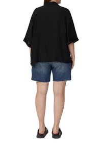 Zwarte, gestikte shirt met korte mouwen en een kraag, gecombineerd met denim short. Schoeisel zijn zwarte instappers. Zicht van achteren.