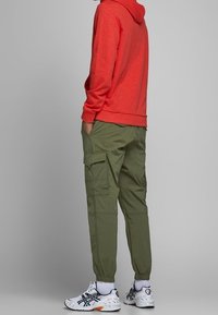 Röd hoodie med känguruficka, olivgröna cargobyxor med sidofickor och vita sportskor med svarta detaljer.