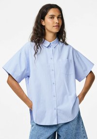 Zilā un baltā svītraina īsām piedurknēm krekls ar pogas leju apkakli, ar krūšu kabatu un brīvu piegriezumu.