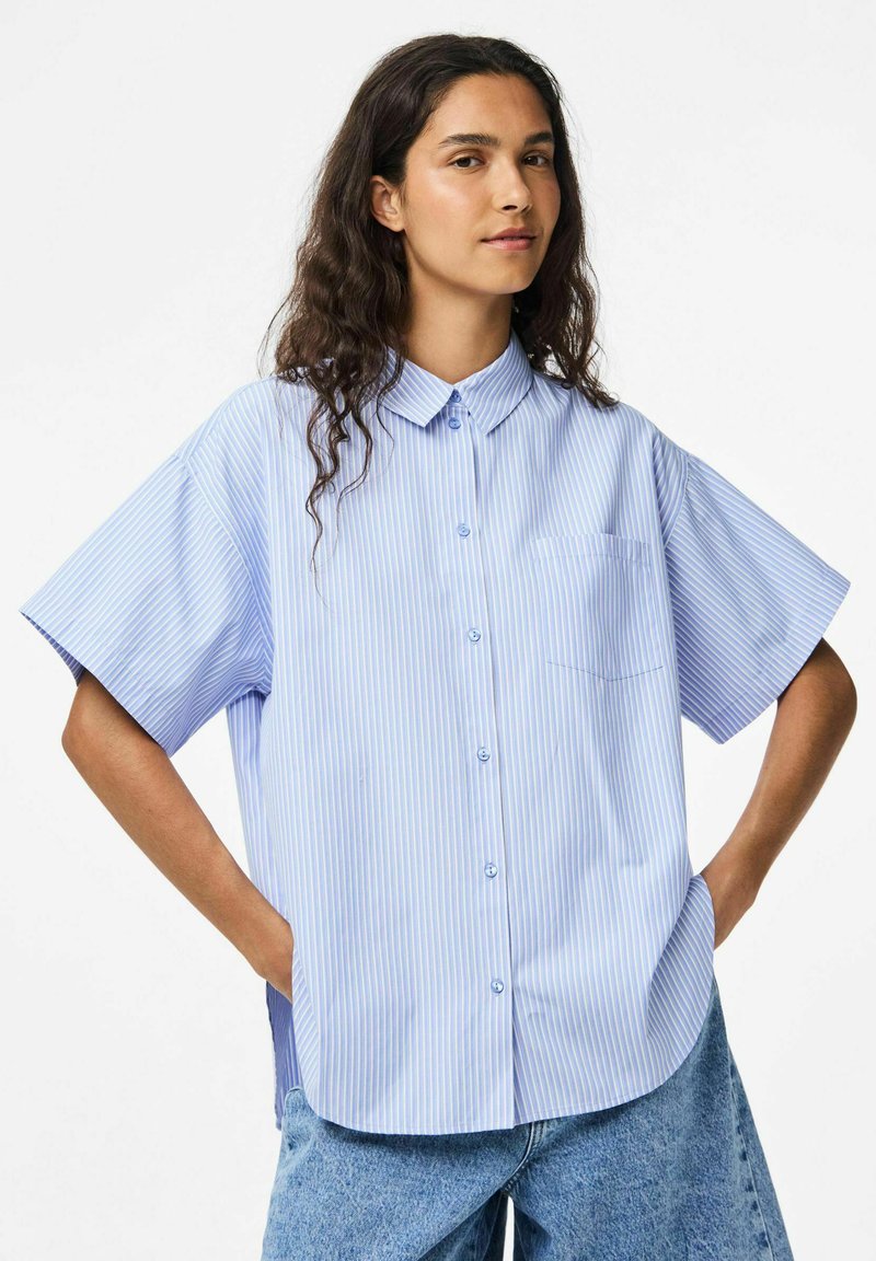 Zilā un baltā svītraina īsām piedurknēm krekls ar pogas leju apkakli, ar krūšu kabatu un brīvu piegriezumu.