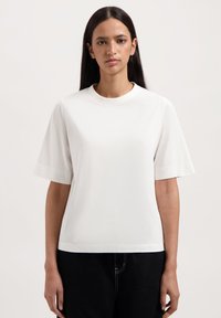 Witte korte mouwen T-shirt van zachte stof, met een ronde halslijn en een subtiel reliëf logo aan de voorkant. Eenvoudige, ontspannen pasvorm.