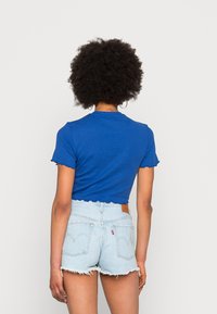 T-shirt bleu à manches courtes, coupé, avec des bords festonnés, associé à un short en denim bleu clair avec des ourlets effilochés et une étiquette en cuir à l'arrière.