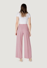 Pantaloni a vita alta e gamba larga di colore rosa chiaro, con pieghe frontali e due tasche posteriori. Il materiale appare liscio con una vestibilità sartoriale.