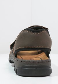 Braune Leder-Sandale mit verstellbarem Riemen, gepolstertem Fußbett und strukturierten schwarzen Sohle. Sichtbare Nähte entlang der Kanten.