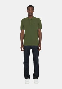 Polo shirt verde oliva con maniche corte, con patta a due bottoni, abbinato a jeans in denim blu scuro e sneakers bianche. Design semplice.