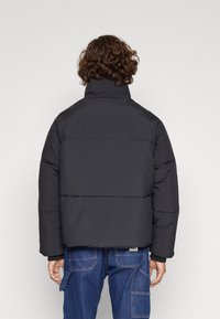 Schwarze Daunenjacke mit hohem Kragen, Reißverschluss und gestepptem Design. Verfügt über eine taillierte Passform und eine glatte, matte Textur.