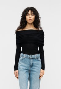 Μαύρο τοπ χωρίς ώμους από απαλό ύφασμα με σχεδιασμό σε πτυχές, σε συνδυασμό με ανοιχτό μπλε τζιν ψηλόμεσο με ζώνη στη μέση.