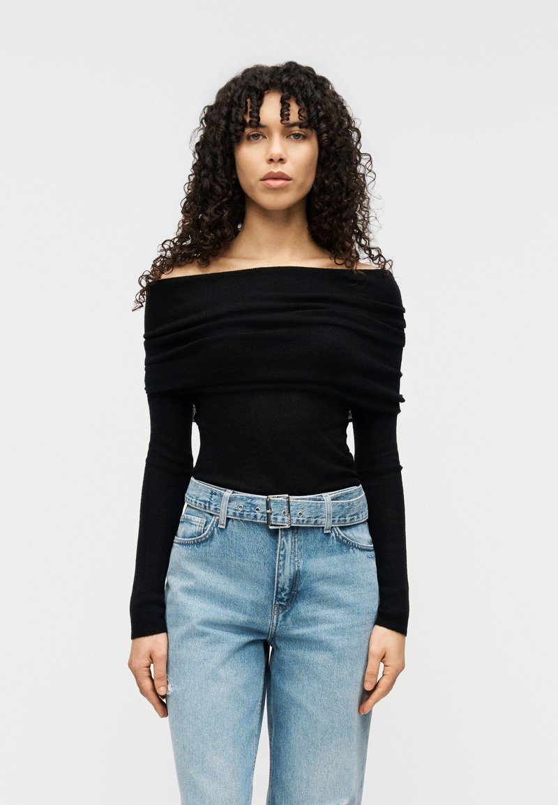 Μαύρο τοπ χωρίς ώμους από απαλό ύφασμα με σχεδιασμό σε πτυχές, σε συνδυασμό με ανοιχτό μπλε τζιν ψηλόμεσο με ζώνη στη μέση.