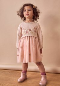 Rosa Tüllkleid mit floralem Stickereien, kombiniert mit einem hellen Strickpullover in Beige. Cremige Stiefeletten mit strukturierter Oberfläche und passenden rosa Socken.