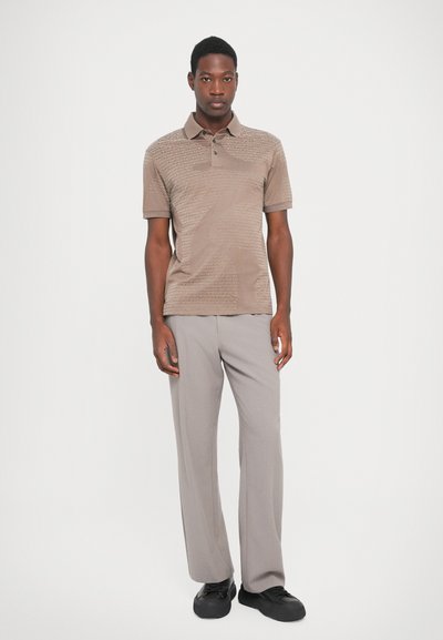 Lys brun polo med teksturert mønster, kortermet; kombinert med lysegrå bukser og svarte joggesko. Enkel og moderne design.