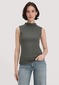 Ärmelloses Oberteil mit hohem Ausschnitt aus dunkelgrünem Rippmaterial. Figurbetonte Form mit leichtem Stretch, kombiniert mit hellblauen Jeans.