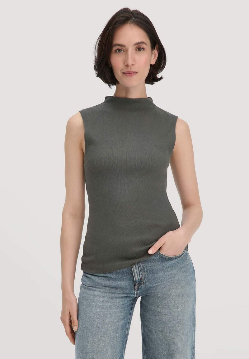 Ärmelloses Oberteil mit hohem Ausschnitt aus dunkelgrünem Rippmaterial. Figurbetonte Form mit leichtem Stretch, kombiniert mit hellblauen Jeans.