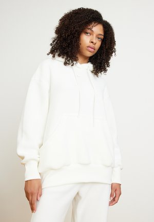 White fleece hoodie with a drawstring hood, front kangaroo pocket, and ribbed cuffs. Soft texture and oversized fit.