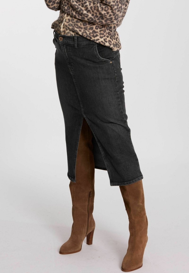 Schwarzer Jeansrock mit hoher Schlitze, klassischem Design, genähten Details und kombiniert mit kniehohen, taupefarbenen Wildlederstiefeln.