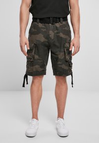 Bermudas en patrón de camuflaje, hechas de tejido duradero. Presentan seis bolsillos, dobladillo ajustable con cuerdas y un cinturón tejido negro. Zapatillas blancas.