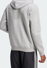 Grå huvtröja med en avslappnad passform, som har en enhetlig textur och ribbade ärmslut. Bärs tillsammans med svarta byxor med vita sidostreck.