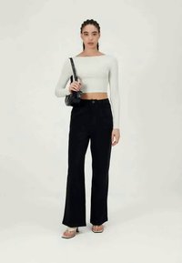 Top branco cropped de mangas longas combinado com calças largas pretas de cintura alta. O modelo leva uma pequena bolsa preta e usa sandálias claras.