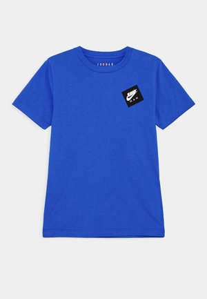 Niebieska koszulka z krótkim rękawem z czarnym kwadratowym logo z napisem "Jump Man" oraz małym logo Nike (swoosh) na lewej części klatki piersiowej.