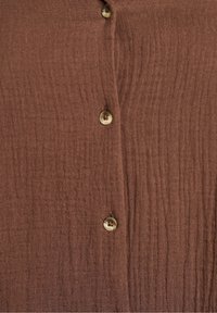 Braun strukturierter Stoff mit dezenten vertikalen Linien, der zwei runde Knöpfe in beigefarbener Nuance aufweist. Nahaufnahme eines Hemd-Frontdesigns.