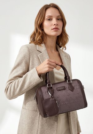 Femme en blazer beige tenant un sac à main marron foncé texturé avec une petite pochette assortie et des ferrures argentées.