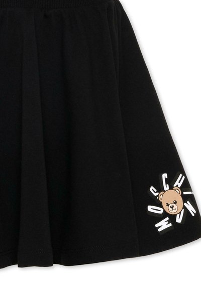 Jupe noire avec une ceinture froncée, ornée d'un petit motif d'ourson et de lettres blanches dispersées près de l'ourlet sur un côté.