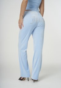 Ljusblå velour träningsbyxor med "Juicy" i strass på baksidan. Har en avslappnad passform och diskret glans, kombinerade med svarta höga klackar.