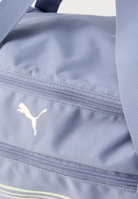 Τμήμα αθλητικής τσάντας σε ανοιχτό μωβ χρώμα που εμφανίζει φερμουάρ και λευκό λογότυπο Puma σε υφασμάτινη επιφάνεια με υφή, με ταιριαστό ιμάντα.