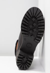 Suola nera con scanalature profonde e motivi incrociati; lato caratterizzato da un accento arancione. Materiale superiore morbido, costruzione robusta, taglia 37.