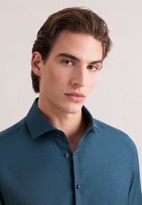 Gestructureerd teal overhemd met knopen en een kraag, met een geometrisch patroon en contrasterende knopen. Soepele stof met een getailleerd ontwerp.