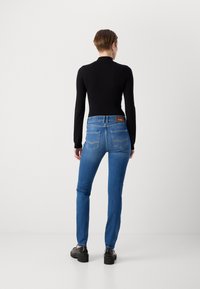 Dunne blauwe denim jeans met een middelhoge taille, voorzien van achterzakken en een bruin leren merklabel. Draag ze met een strakke zwarte top en zwarte schoenen.