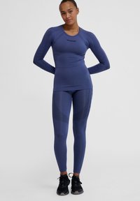 Athletic set i mörkblått; långärmad topp med texturerade accent och matchande högmidjade leggings med geometriska mönster. Stretchtyg.