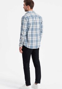 Geruit overhemd met knopen in lichtblauw en wit, met lange mouwen en een gebogen onderkant. Gecombineerd met zwarte slim-fit broek en witte sneakers.