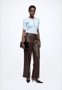 Svetlo modra rebrasta majica s kratkimi rokavi in gumbi, kombinirana s širokimi rjavimi hlačami iz umetnega usnja ter črno torbico; model nosi črne pete.