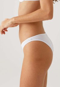 Witte katoenen bikini slipjes met een lage taille, voorzien van een zachte elastische tailleband en een gladde textuur, zijwaarts weergegeven.