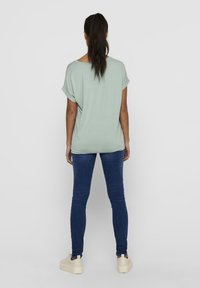 Mintgrünes, locker sitzendes T-Shirt mit umgeschlagenen Ärmeln, kombiniert mit dunkelblauen engen Jeans und weißen Plateausneakern, von hinten betrachtet.