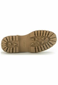 Brązowa gumowa podeszwa buta z głębokim bieżnikiem, z wzorami w kształcie strzał, logo marki i teksturowaną powierzchnią dla lepszej przyczepności.