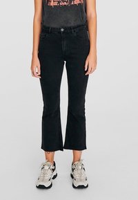 Jeans neri a campana con orlo grezzo, realizzati in denim, con vita alta e dettagli di cucitura minimi. Abbinati a sneaker di colore neutro.