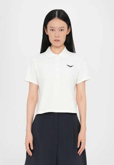 Weißes Poloshirt mit Kragen, kurzen Ärmeln und crop Design. Mit einem kleinen dunklen gestickten Emblem auf der linken Brust.